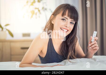 Junge schöne Frau, die einen Schwangerschaftstest abhält. Ein positives Ergebnis. Er ist glücklich, weil er eine Mutter sein wird. Stockfoto