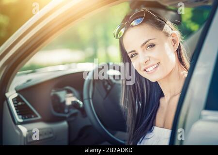 Schöne junge Frau, die mit einem Lächeln im Innenraum eines neuen Autos sitzt. Er ist froh, dass er ein Fahrer ist. Stockfoto