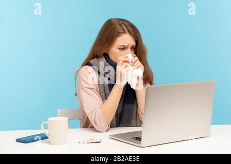 Weibliche Büroleiterin niest Husten in Gewebe, fühlt sich beim Arbeiten am Schreibtisch am Laptop unwohl, leidet an Fieber, saisonaler Beeinflussung Stockfoto