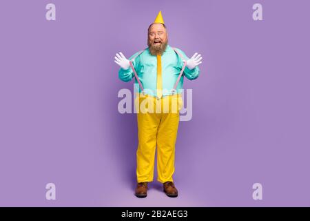 Foto in voller Größe von aufgeregt fröhlichem fetten Mann ziehen seine rosafarbenen Hosenträger genießen Jubiläumsfeier tragen Cone Hose türkis Schuhe isoliert Stockfoto