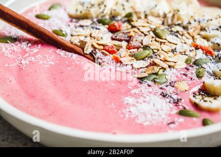 Acai Smoothie Schüssel mit Granola, Früchten und Samen in einer weißen Platte, grauer Hintergrund. Gesundes veganes Lebensmittelkonzept. Stockfoto