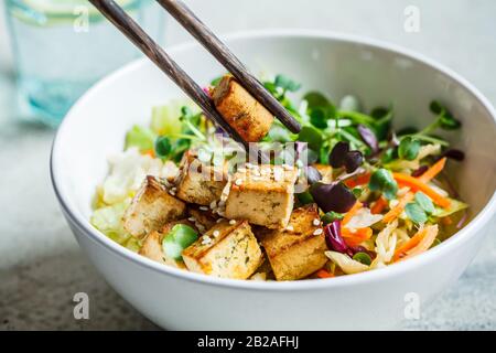 Gebratener Tofusalat mit Sprossen und Sesamsamen in einer weißen Schüssel. Veganes Essen, asiatisches Speisekonzept. Stockfoto