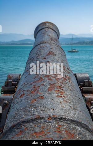 Antike alte Kanone, die mit verschwommenem Boot auf das Meer zeigt Stockfoto