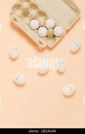Frohe Ostern. Weiße Eier mit bemalten Augen in Papierverpackungen auf gelbem Hintergrund. Flaches Layout, Draufsicht, Kopierbereich. Stockfoto