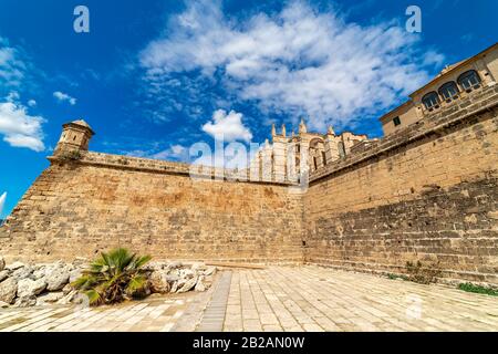 Berühmte Kathedrale von Santa Maria und die umliegende mittelalterliche Mauer unter dem blauen Himmel in Palma de Mallorca, Spanien. Stockfoto