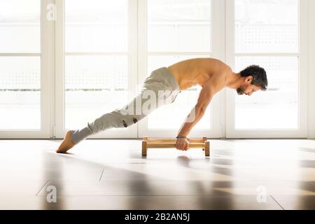 Muskulöser sportlicher Mann, der eine planche Kalisthenikplanche macht, posieren auf niedrigen parallelen Bodenleisten in einem hellen, geräumigen Fitnessstudio mit Kopieraum für Gesundheit und Fitness c Stockfoto