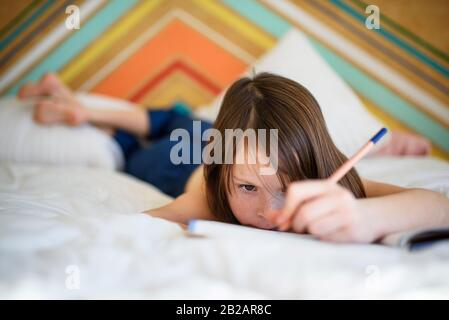 Portrait eines Mädchens, das auf ihrem Bett liegt und seine Hausaufgaben macht Stockfoto