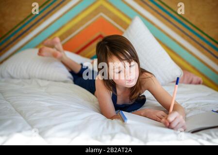 Portrait eines Mädchens, das auf ihrem Bett liegt und seine Hausaufgaben macht Stockfoto