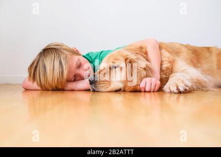 Junge, der auf dem Boden liegt und einen goldenen Hund umknudelt Stockfoto