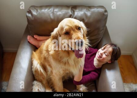 Glückliches Mädchen in einem Sessel mit goldenem Retriever Stockfoto