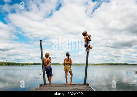 Drei Kinder, die auf einem Dock stehen und dabei angeln und sich darüber durcheinander bringen, USA Stockfoto