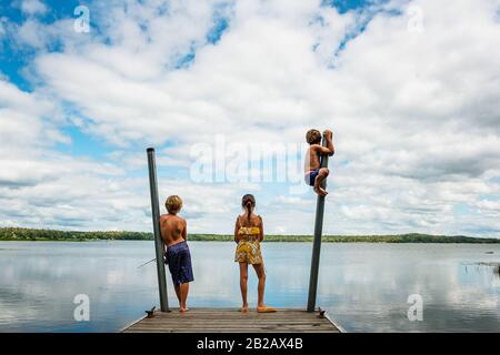 Drei Kinder, die auf einem Dock stehen und dabei angeln und sich darüber durcheinander bringen, USA Stockfoto