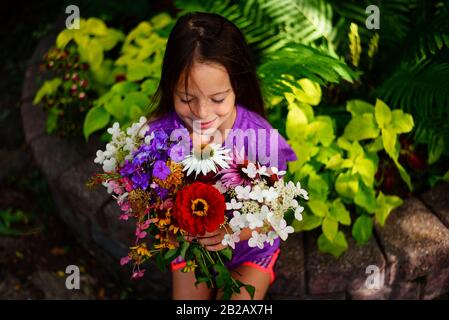 Porträt eines lächelnden Mädchens, das in einem Garten sitzt, der einen Haufen Blumen hält, USA Stockfoto