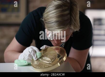 Royal Mint Designerin Laura Clancy, Polieren einer Blechnachbildung einer einzigartigen 7 Kilo Gold James Bond Münze, die sie entworfen hat - die größte Münze mit dem höchsten Nennwert, die in der 1.100-jährigen Geschichte des Mint produziert werden soll - während der Einführung einer neuen James Bond Münze und Goldbar-Sammlung im Voraus Von der Veröffentlichung des 25. James-Bond-Films "No Time To die" in der Ausstellung "Bond in Motion" im London Film Museum, London. PA Foto. Bilddatum: Montag, 2. März 2020. Siehe PA Story MONEY Bond. Der Fotokredit sollte lauten: Yui Mok/PA Wire Stockfoto