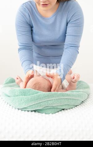 Gesichtsmassage für Babys. Mutter streichelt sanft mit beiden Händen das Gesicht des Babyjungen. Nahaufnahme mit zugeschnittenen Aufnahmen. Stockfoto