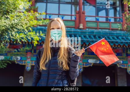 Urlaub in China genießen. Junge Frau in medizinischer Maske mit chinesischer Nationalflaggen auf dem Hintergrund der alten chinesischen Straße. Reisen Sie nach China Stockfoto