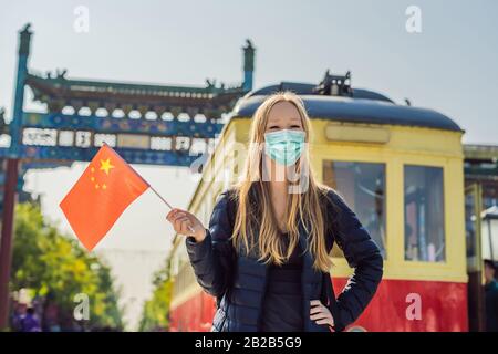 Urlaub in China genießen. Junge Frau in medizinischer Maske mit chinesischer Nationalflaggen auf dem Hintergrund der alten chinesischen Straße. Reisen Sie nach China Stockfoto