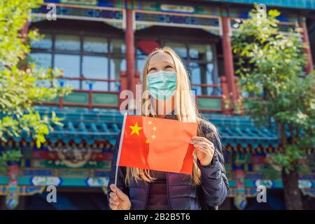 Urlaub in China genießen. Junge Frau in medizinischer Maske mit chinesischer Nationalflaggen auf dem Hintergrund der alten chinesischen Straße. Reisen Sie nach China Stockfoto