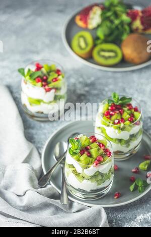 Gesundes Frühstück: Joghurt parfait mit Granola und Kiwi Dekoration Granatapfel und Minze auf grauem Hintergrund. Stockfoto