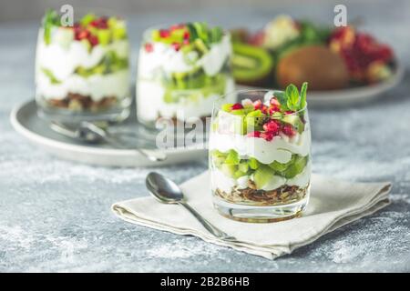 Kiwi Parfait Dessert aus Glas mit Zutaten. Joghurt, Granola und Obst. Gesunder Snack oder Frühstück. Hellgraue Betonoberfläche. Stockfoto