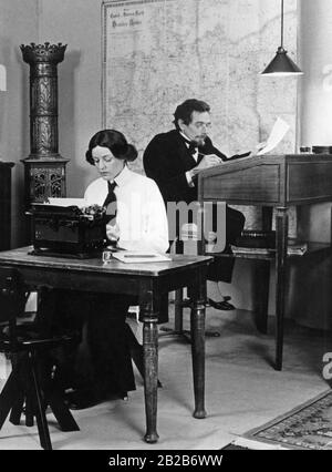 Umbau eines vor 1914 im Bürostil der Zeit eingerichteten Handelsbüros mit Hochstuhl, hohem Schreibtisch und Schreibmaschine, auf dem die Büroangestellte tippt. An der Wand hängt eine Karte des Deutschen Reiches. Stockfoto