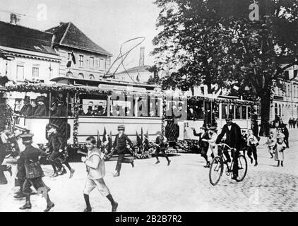 September 1907 die erste elektrische Straßenbahn in Potsdam bei ihrer feierlichen Eröffnung. Zwischen Hauptbahnhof, Sanssouci und Bahnhof Charlottenburg verlief die Strecke mit Förderwagen der Firma "Gottfried Lindner AG". Kinder gehen neben der Straßenbahn, die mit Blumen und Fahnen dekoriert ist. Stockfoto