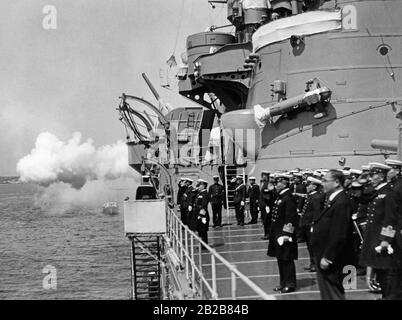 Der Kreuzerkreuzer Ashigara der Kaiserlich japanischen Marine besucht die Kieler Woche. Die Besatzung ist auf dem Deck aufgereiht. Eine Waffe wird zu Ehren des deutschen VizeAdmiral Carls abgefeuert, der mit seinem Boot auf dem Schiff mooren. Stockfoto