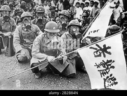 Eine Gruppe japanischer Soldaten quietschte während einer luftangriffübung auf einer Straße in einer japanischen Stadt. Sie tragen Gasmasken und Fahnen. Im Hintergrund Zuschauer aus der Stadt. Stockfoto