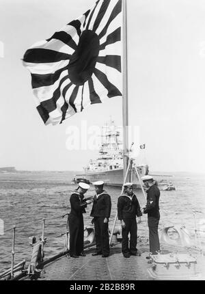 Am Bug des Kreuzers Ashigara der Kaiserlich japanischen Marine in Kiel unterhalten sich vier deutsche und japanische Seeleute. Im Hintergrund das gepanzerte Schiff Admiral Graf Spee. Stockfoto