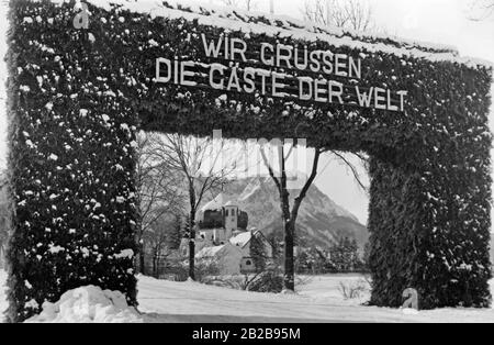 Ehrenpforte im Skistadion in Garmisch-Partenkirchen. Dort werden die Olympischen Winterspiele 1936 ausgetragen. Im Hintergrund steht eine Kirche. Stockfoto