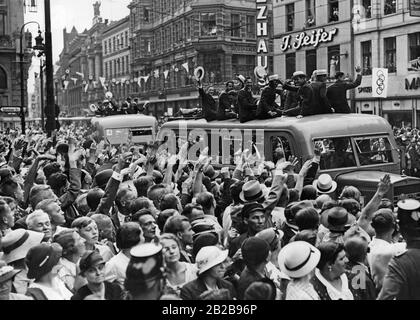Olympischen Sommerspiele in Berlin: Ankunft des amerikanischen Olympiateams vor dem Rathaus. Die Athleten sitzen in einem Bus, winken mit ihren Hüten und werden von einer Menschenmenge begrüßt. Stockfoto
