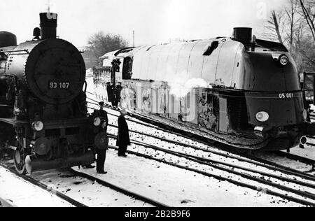 Die erste Fahrt der Schnellzuglok der Klasse 05 (05001) der Deutschen Eisenbahn auf der Strecke Richtung Tegel. Sie wurde in der Lokfabrik Borsig in Tegel gebaut und hatte eine Höchstgeschwindigkeit von 170 km/h. Auf dem Nebengleise befindet sich eine Dampflok mit der Nummer 93107, dazwischen Bahnangestellte. Stromlinienförmige Dampfloks vor 1945, Lokomotiven: Historisch, Eisenbahn. Stockfoto