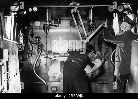 Suchen Sie im Führerhaus einer Dampflok. Ein Zugführer beim Betrieb der Mechanik und ein Feuerwehrmann, der den Kessel anstochen. Stockfoto