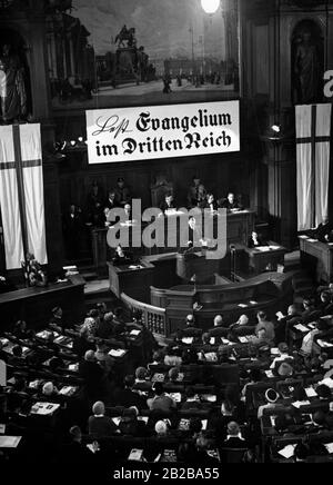 Im Herrenhaus in der Leipziger Straße findet die Reichstreferenz der religiösen Bewegung Deutsche Christen statt. Das Foto gibt während der Rede von Pfarrer Peter zum Thema "Kirche und Menschen" einen Blick in den Versammlungsraum. Über dem Podium hängt ein Banner mit dem Slogan: "Im Dritten Reich das Gospel lesen". Rechts sitzen die Ehrengäste der Kirche. Stockfoto