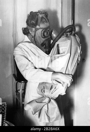 Um Babys vor Gas zu schützen, wurden zahlreiche Forschungen durchgeführt. Dr. Le-Mee vom Krankenhaus Halskette-Enfants-Malades von Hopital entwarf ein tragbares Gerät aus einem Material, das Gas nicht durchdringen kann. Der Säugling kann in diesem Gerät transportiert werden. Seine Atmung wird durch ein Rohr gewährleistet, das mit der Gasmaske des Trägers/der Mutter verbunden ist. Auf dem Bild präsentiert eine Krankenschwester den Apparat. Stockfoto