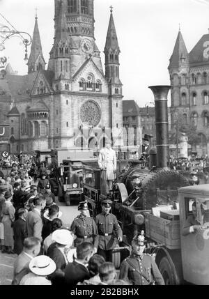 Der Nachbau der ersten deutschen Lok "Adler" wird in die Messehallen am Kaiserdamm in Berlin transportiert. Der Lastwagen mit der Lok fährt vor der Kaiser-Wilhelm-Gedächtniskirche vorbei, die im Hintergrund zu sehen ist. Viele Menschen stehen am Straßenrand. Auf der Lok steht ein SA-Mann in weißem Mantel. Der Zug wird von SS-Männern mit Hakenkreuzen und Polizisten begleitet. Stockfoto