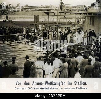 Athleten starten im modernen Pentathlon beim 300-Meter-Schwimmwettbewerb. Zuschauer sehen vom Poolrand aus. Die Konkurrenten sind Mitglieder des deutschen Militärs und absolvieren ihren Sportdienst. Stockfoto