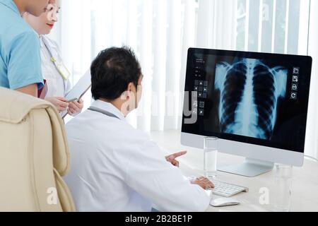 Pulmonologe und seine Assistenten untersuchen den Röntgenstrahl des Patienten auf dem Computerbildschirm Stockfoto