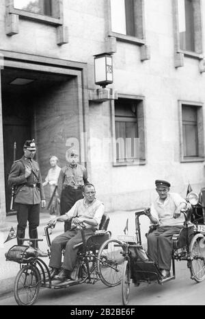 Zwei Kriegsinvaliden mit ihrem Dreirad vor der Staatskanzlei. Sie fuhren von Hindenburgs in Obermösien nach Berlin, um von Bundeskanzler Adolf Hitler empfangen zu werden. Ein Polizist und ein SS-Mann bewachen den Eingang. Stockfoto