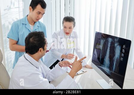 Die Ärzte versammelten sich am Schreibtisch, um den schwierigen Fall einer Lungenentzündung zu besprechen und die Röntgenuntersuchung der Patienten zu überprüfen Stockfoto