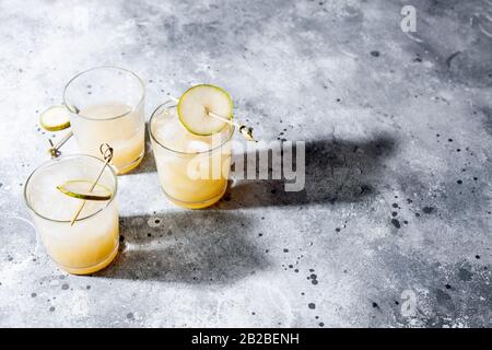 Cold-Birne-Cocktail oder Mocktail mit Soda- und Birnpüree und Fruchtscheiben in kurzem Glas auf grauem Hintergrund mit Schatten. Erfrischendes Sommergetränk Stockfoto