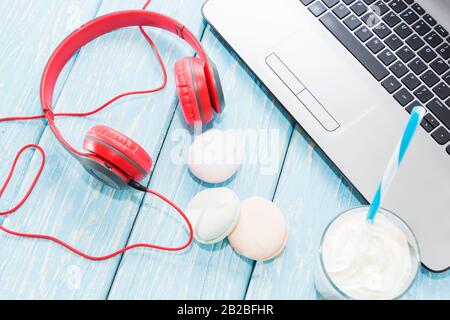 Offener Laptop mit weißem Kaffeetup, Marshmallows und roten Kopfhörern Stockfoto