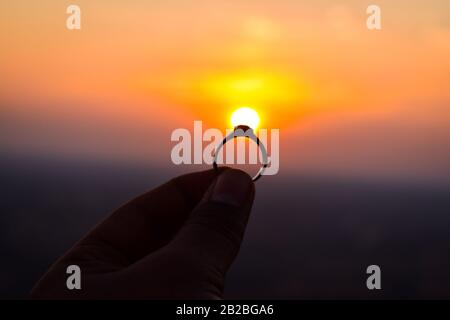 Ein schöner Ring in der Hand gehalten, um Sonne vorzuschlagen. Die Sonne wirkt wie der Diamant des Rings Stockfoto