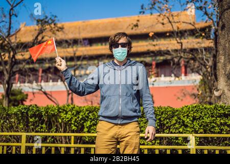 Urlaub in China genießen. Junger Mann in medizinischer Maske mit nationaler chinesischer Flagge in Verbotener Stadt. Reise nach China Konzept. Touristen fürchten 2019 Stockfoto