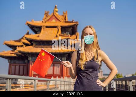 Urlaub in China genießen. Junge Frau in medizinischer Maske mit chinesischer Nationalflaggen in Verbotene Stadt. Reise nach China Konzept. Touristen fürchten 2019 Stockfoto