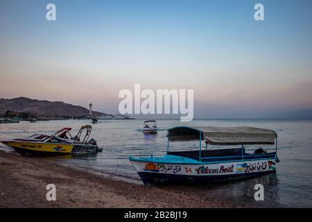 Aqaba, JORDANIEN - 31. JANUAR 2020: Sehr früh morgens warten Glasboote auf neugierige Touristen, Strand der Stadt. Winter klarer Urlaubshimmel um Sonnenaufgang. Rotes Meer, Haschemitisches Königreich Jordanien Stockfoto