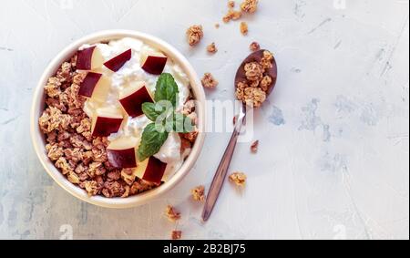 Granolatschüssel mit Joghurt, geschnittenen Äpfeln und Basilikum auf strukturiertem weißem Tisch. Gesundes Frühstück. Draufsicht. Platz für Text kopieren. Stockfoto