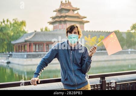 Urlaub in China genießen. Junger Mann in medizinischer Maske mit nationaler chinesischer Flagge in Verbotener Stadt. Reise nach China Konzept. Touristen fürchten 2019 Stockfoto