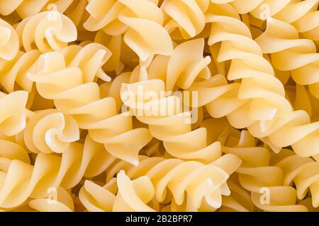 Rohe getrocknete Fusilli-Pasten auf Pfahldetails als gelb strukturierter Hintergrund. Extrudierte, spiralförmige Rotini Weizenpastas. Enthalten Saccharid, Stärke und Gluten. Stockfoto
