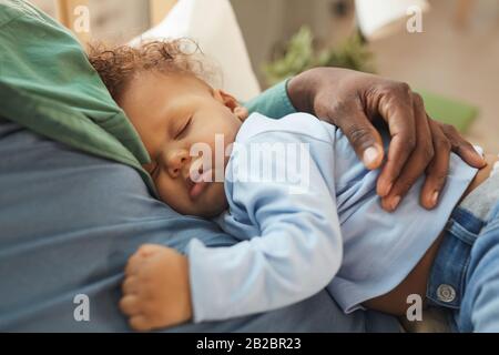 Hochwinkeliger Blick auf das niedliche Mixed-Race-Baby, das in den Armen der Väter schläft Stockfoto
